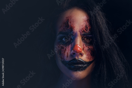 Portrait of spooky evil joker with scary makeup at dark photo studio.