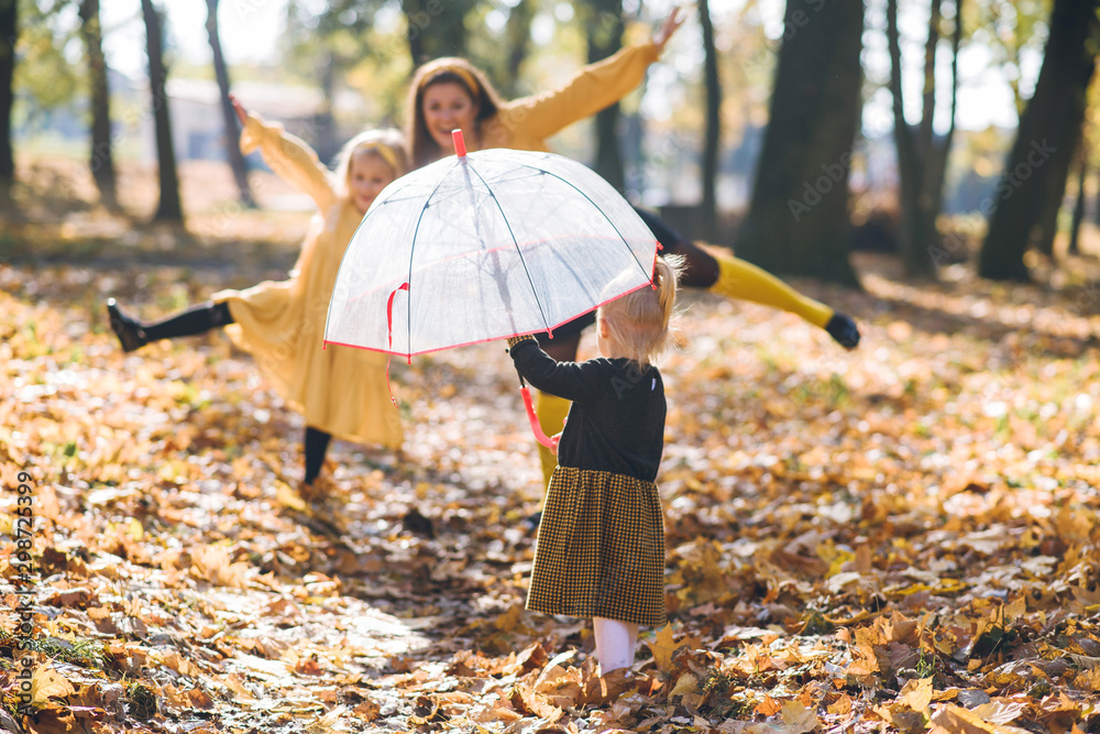 mom with two little daughters in yellow clothes walking in the autumn park