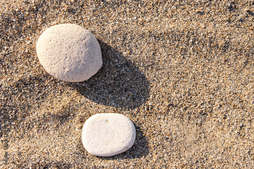 Two white pebble stones on the sand. Sunset photo with long shadows. Two white pebble stones on the sand. Sunset photo with long shadows.