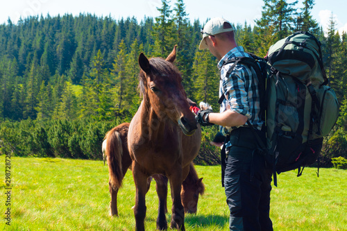 guy stroking and feeds a horse in the mountains