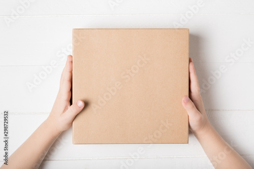 Square cardboard box in children hands. Top view, white background photo