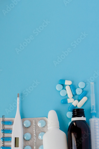 Treatment of colds and flu. Various medicines, a thermometer, sprays from a stuffy nose and a pain in a throat on a blue background. Copy space. Medicine flat lay