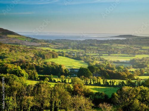 Country landscape in Burren region of Ireland  Galway bay in background  Blue cloudy sky  Green fields and trees.