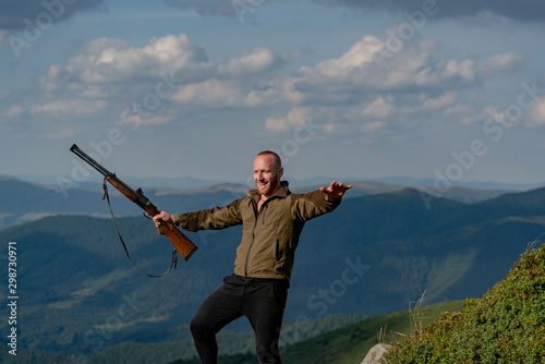 Hunting - Men hobby. Excited Hunter with Powerful Rifle with Scope Spotting Animals. Male with a gun. A hunter with a hunting gun hunt in summer forest.