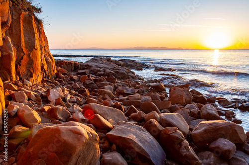Scenic rocky beach Cala Violina landscape at the sunset. The sun is going down behind the horizon. Tyrrhenian Sea bay at the sunset. photo