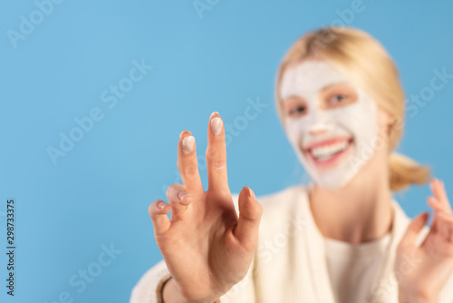 Beautiful young woman applying moisturizing cream at face using two fingers and smile. Healthy and wellness concept. Blured healthy girl doing skin care routine.