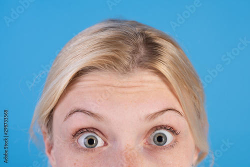 Surprised young blonde woman with blue eyes and thin brows over bright blue background. Selfcare and beauty concept. Close up portrait of shoked blonde girl. photo