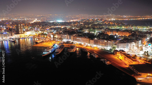 Aerial drone night shot of beautiful illuminated port of Piraeus and huge cruise liner departing to Aegean popular destinations, Attica, Greece