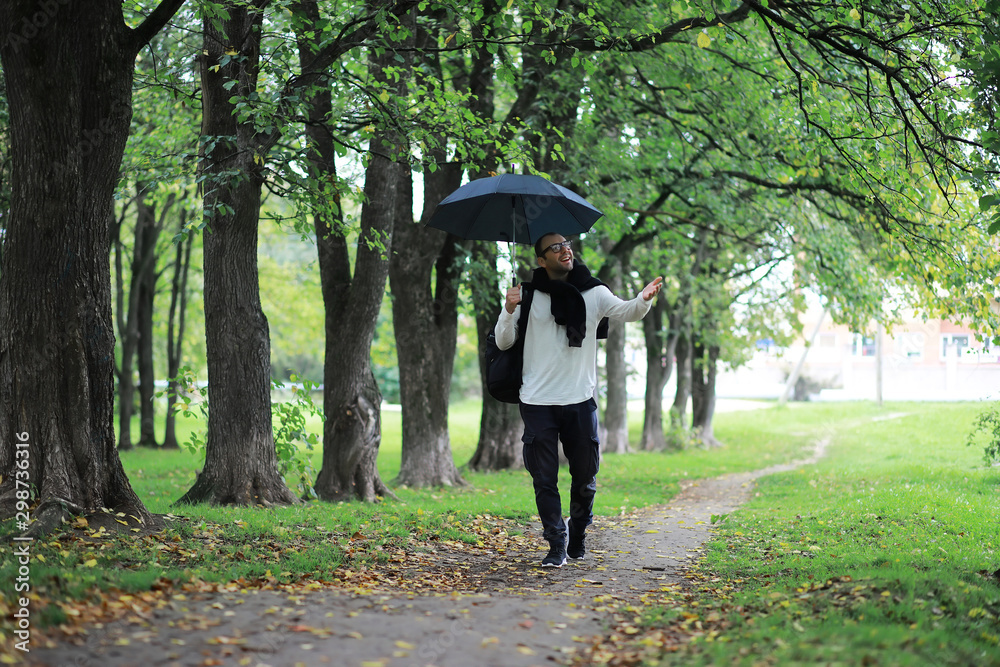 A young man in glasses walks in the park with an umbrella during the rain. A young man in glasses walks in the park with an umbrella during the rain.