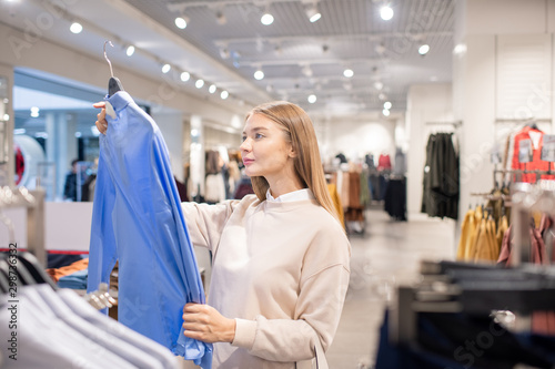 Casual blonde woman looking at blue shirt in clothing department