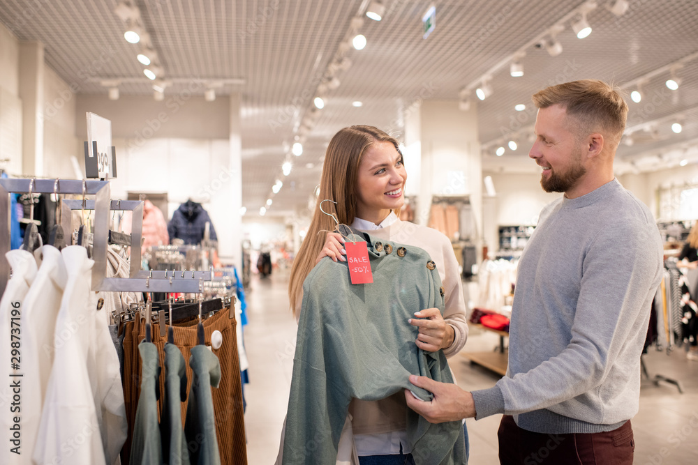 Happy girl looking at her boyfriend while pointing at grey knitted pullover Happy girl looking at her boyfriend while pointing at grey knitted pullover