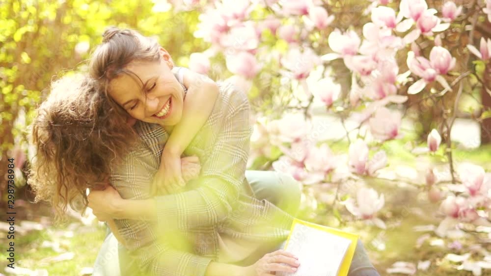 Happy teenage boy hugs his beautiful young mother. Spring portrait on a background of blooming pink magnolia. Mothers Day Happy teenage boy hugs his beautiful young mother. Spring portrait on a background of blooming pink magnolia. Mothers Day