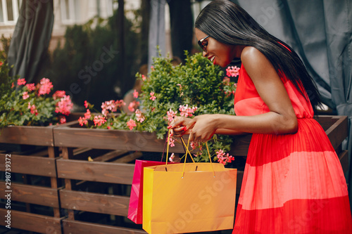 Black girl in a summer city. Woman with a shoping bags. Lady in a red ress photo