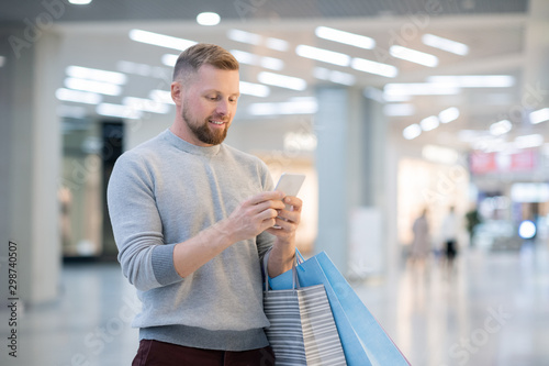 Young man with paperbags and smartphone looking at promo on screen