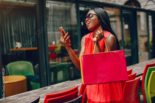 Black girl in a summer city. Woman with a shoping bags. Lady in a red ress photo