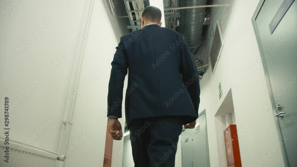 man in suit walks along hallway backside low angle view