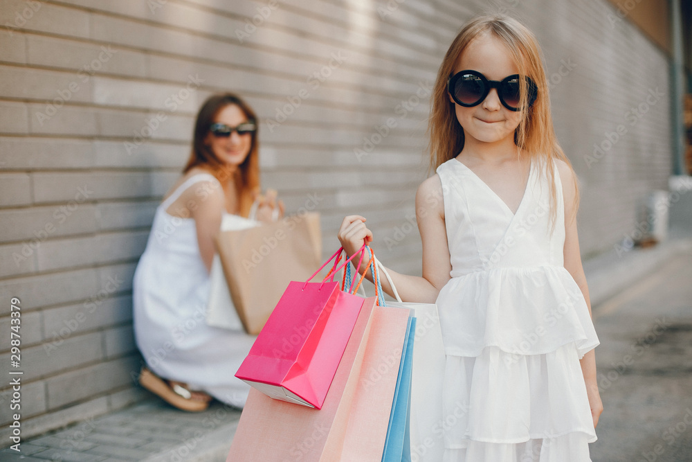 Beautiful girl in a summer city. Lady with shopping bags. Mother with daughter in stylish clothes Beautiful girl in a summer city. Lady with shopping bags. Mother with daughter in stylish clothes