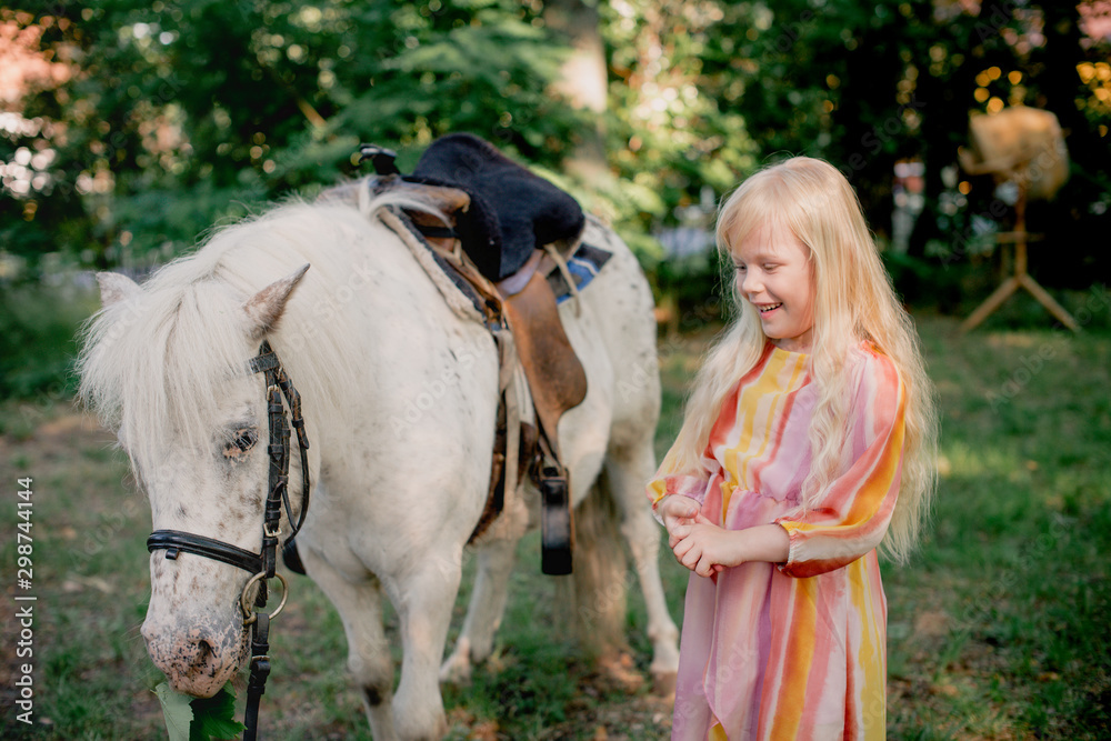 Fototapeta premium kleines blondes Mädchen, das ein Pony füttert 
