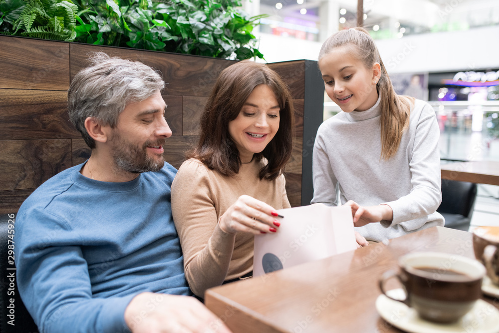 Young woman taking look at gift in paperbag with daughter and husband near by