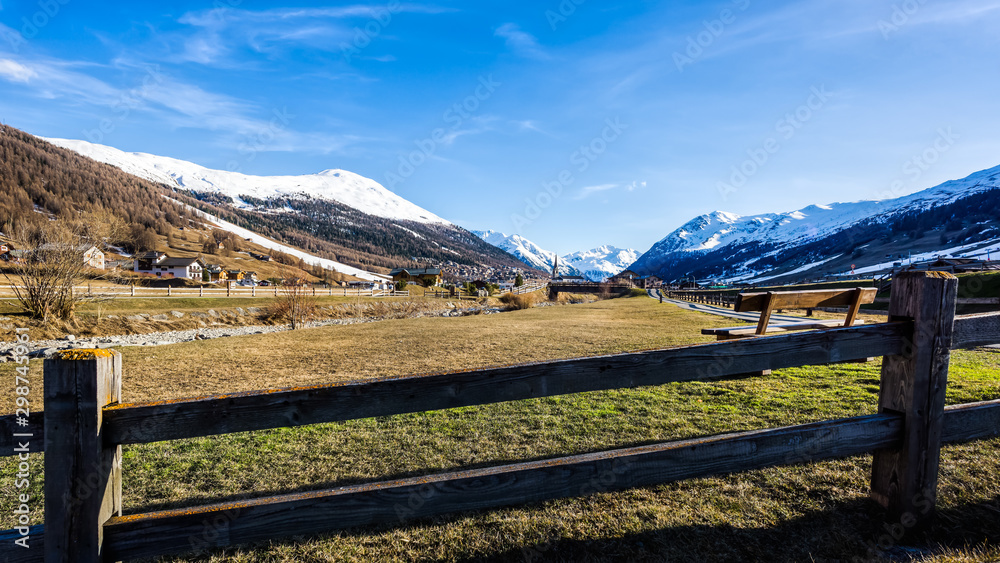 Mountain valley with stream, wooden fence and footpath, Livingo village and slopes, Italy, Alps