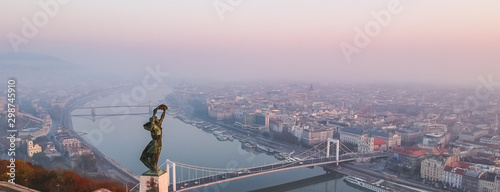 Photography Aerial view to the Statue of Liberty with Elisabeth Bridge and River Danube taken from Gellert Hill on sunrise in fog in Budapest, Hungary