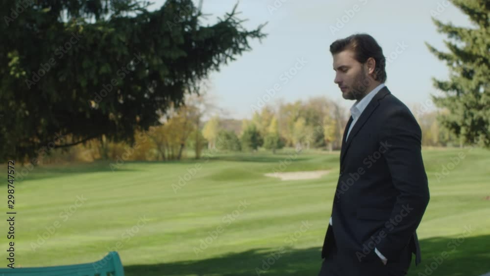 Cute guy getting acquainted with a young fair-haired girl in a park. A woman sits on a bench and uses her smartphone. A man begins a conversation with her. Cute guy getting acquainted with a young fair-haired girl in a park. A woman sits on a bench and uses her smartphone. A man begins a conversation with her.