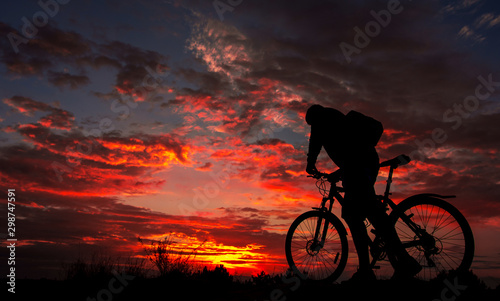 cyclist with a bicycle, in the background fiery sunset. © Lumppini