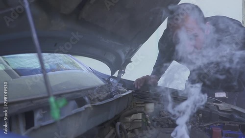 A man is very frustrated while trying to evaluate his smoking car engine.