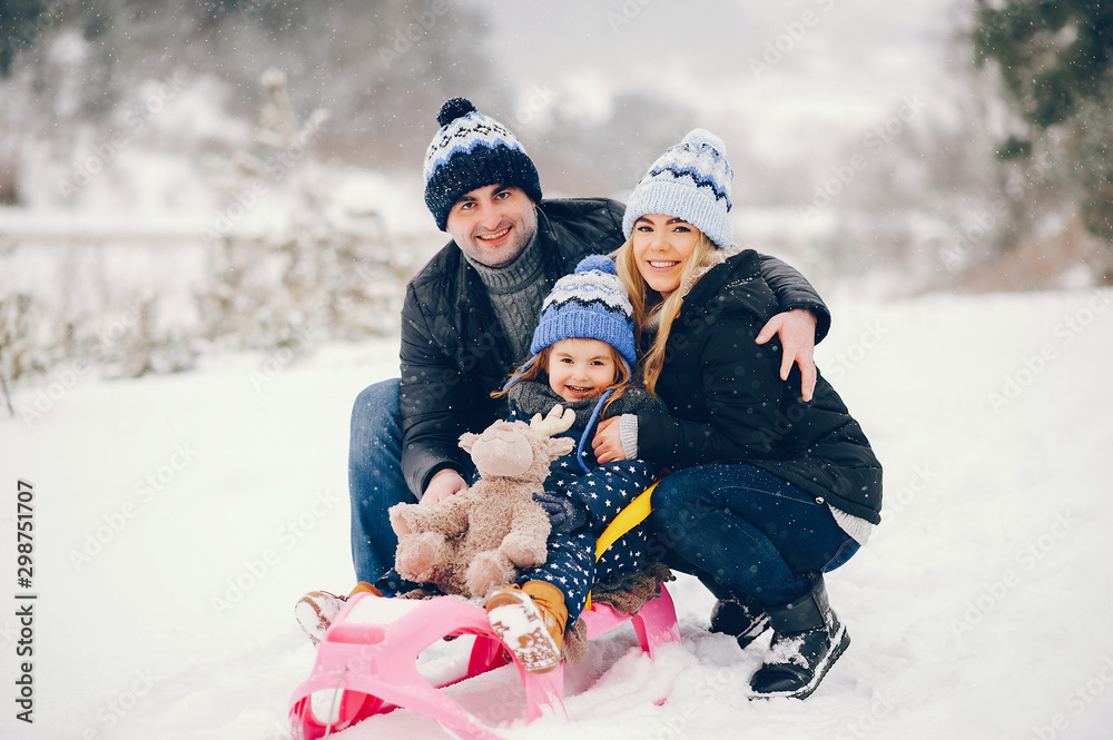 Family have fun in a winter park. Stylish mother in a blue jacket. Little girl on a pink sled. Father with cute daughter