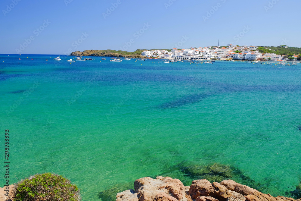 View on the blue lagoon and the village Es Grau with white houses on Menorca.