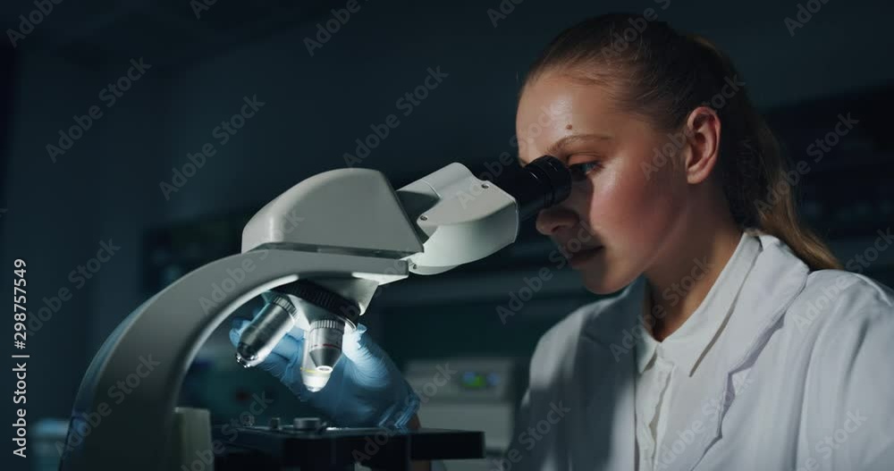 Portrait of blond female scientist is analyzing a sample to extract the DNA and molecules with microscope in laboratory.