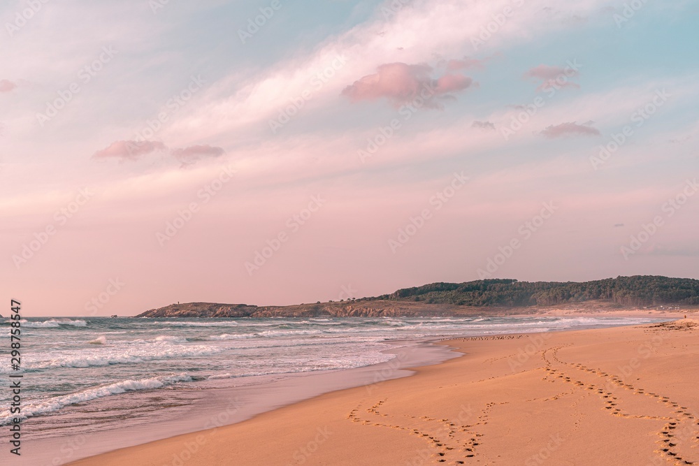 Playa idílica y solitaria en otoño con línea de huellas con cielo de hermosas nubes rosadas