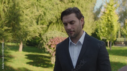 A handsome young guy of European appearance with a slight unshavenness in a business suit is walking in the park. A man calls and expresses surprise photo