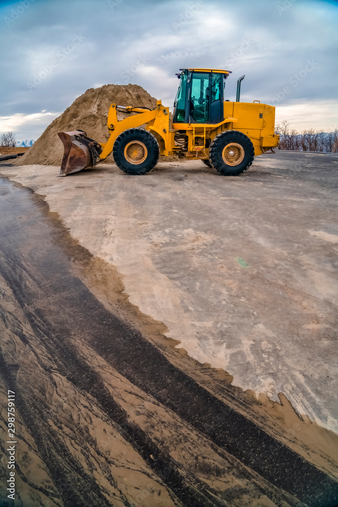 Yellow bulldozer on a road with mound of soil and cloudy sky background Yellow bulldozer on a road with mound of soil and cloudy sky background