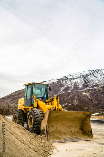 Front of a yellow bulldozer against snowy mountain and cloudy sky in winter