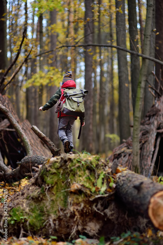 Little boy scout with backpack and rope during hiking in autumn forest. Behind the child is teepee hut.