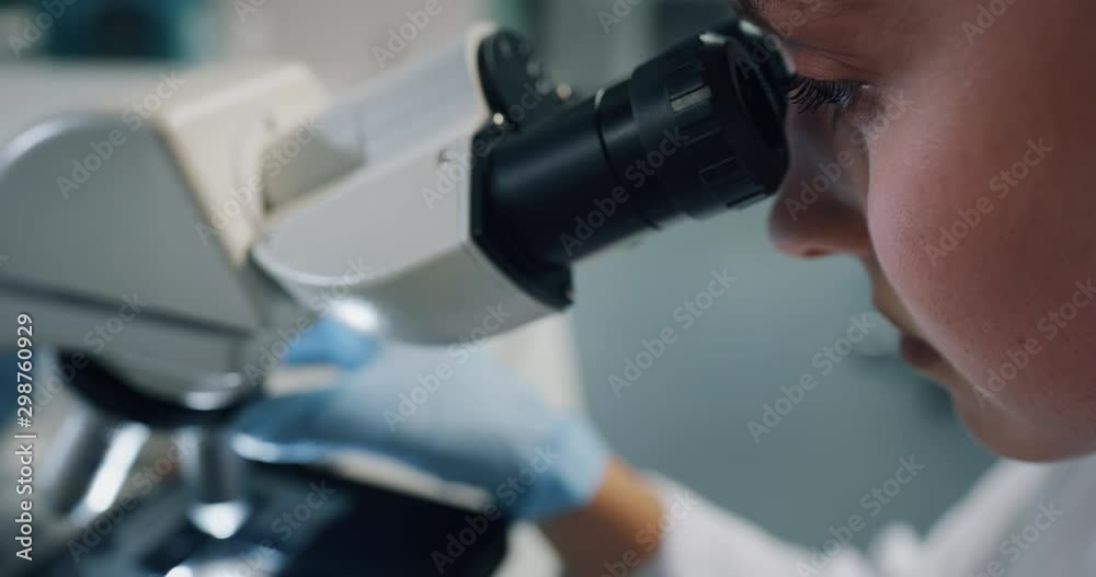 Close up shot of blond female scientist is analyzing a sample to extract the DNA and molecules with microscope in laboratory.