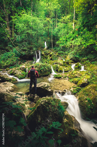 man with backpack sits on stone at a waterfall in the forest and meditates alone