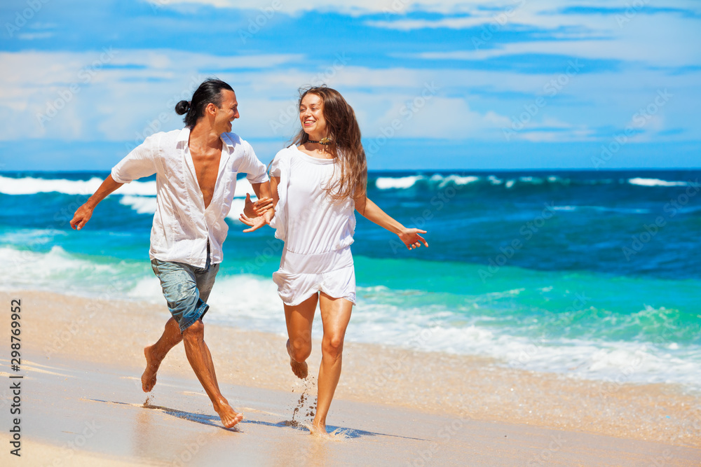 Happy family on honeymoon holiday - just married young couple having fun, run by water edge along sea beach surf. Active lifestyle, people recreational activity on summer vacation on tropical island.