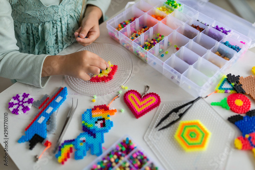 Cute little girl makes a toy with thermo mosaic. Development, modeling, education, design with hot plastic. Modern technologies. DIY.