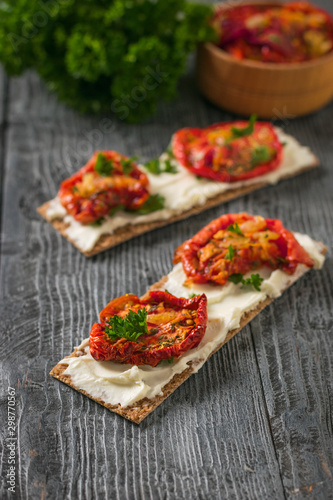 Cream cheese and sun-dried tomatoes on bread toast on a wooden table.