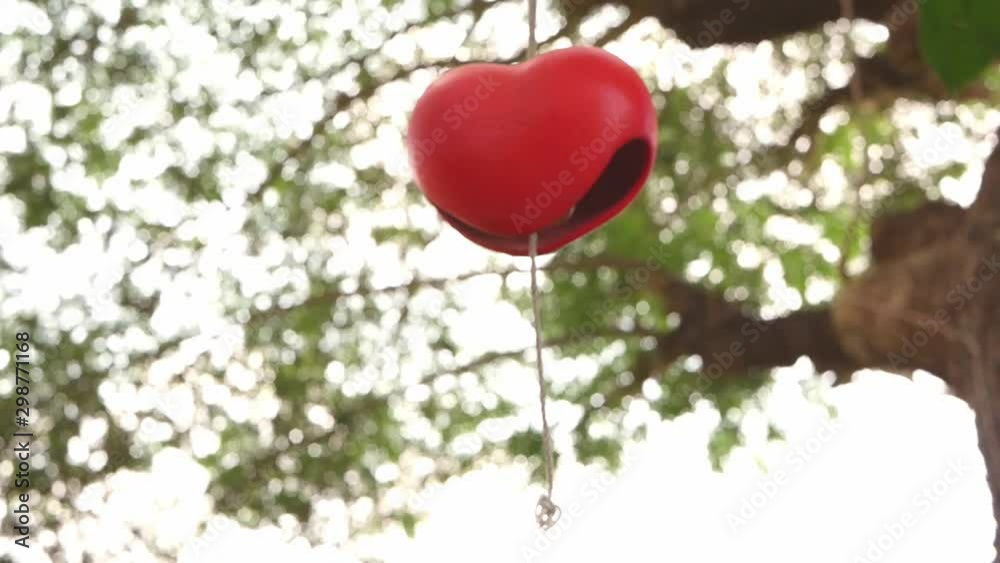 Woman caught red heart shape ceramic wind chimes hanging on a branch of tree in the garden. Woman caught red heart shape ceramic wind chimes hanging on a branch of tree in the garden.
