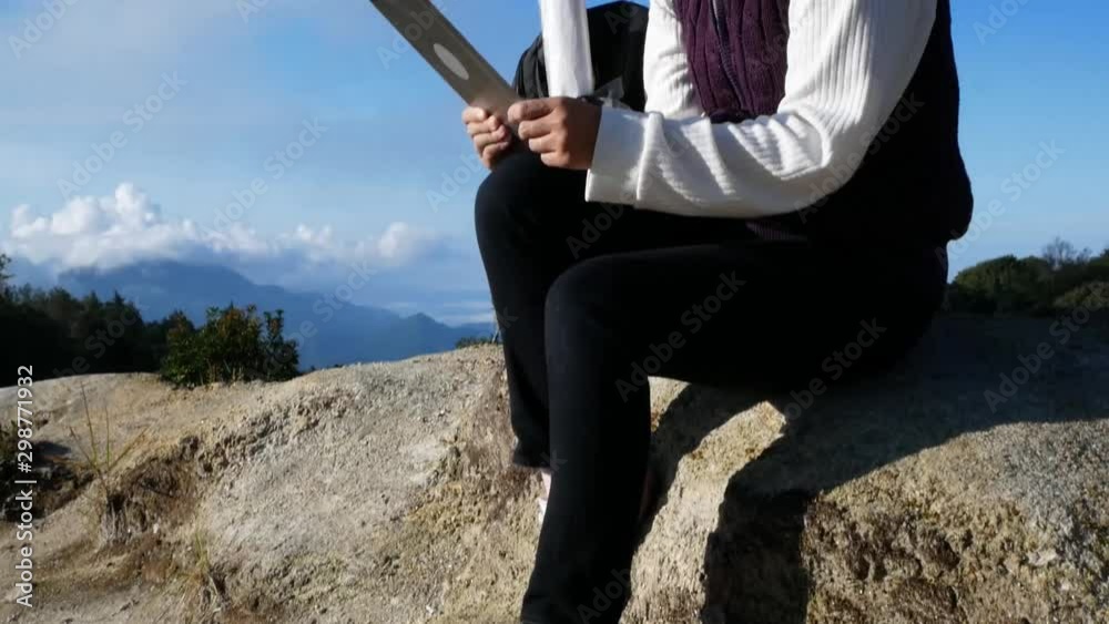 Young woman traveler sitting on the rock and searches GPS coordinates on tablet at peak of Inthanon mountain in morning on summer vacations day. Lifestyle hiking concept. Young woman traveler sitting on the rock and searches GPS coordinates on tablet at peak of Inthanon mountain in morning on summer vacations day. Lifestyle hiking concept.