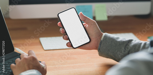 Cropped shot of young businessman holding blank screen smartphone while working on his project