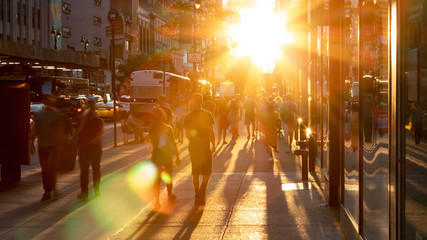 Sunlight shines on the diverse crowds of people walking down the busy sidewalk on 34th Street through Midtown Manhattan in New York City