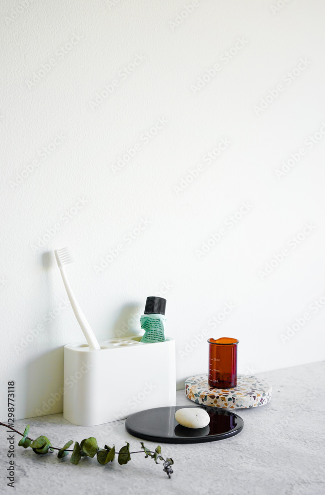 Bathroom amenities in minimal style on white wall background concrete table top. Stylish and modern trendy room interior decoration. Toothbrush, toothpaste, plant, stone, terrazzo, concrete elements. Bathroom amenities in minimal style on white wall background concrete table top. Stylish and modern trendy room interior decoration. Toothbrush, toothpaste, plant, stone, terrazzo, concrete elements.