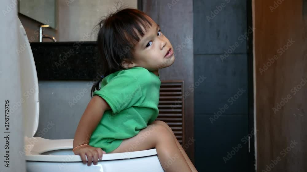 Adorable Asian child girl sitting on toilet bowl at home in the morning. Health care concept. Adorable Asian child girl sitting on toilet bowl at home in the morning. Health care concept.