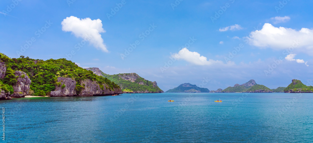 Tourist kayaking in blue Idyllic turquoise ocean to explore near the island with lush green jungle trees and lime stone mountains at Ang Thong National Marine Park, Thailand.