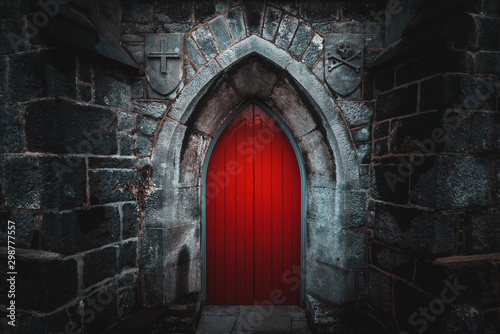 Scary pointy red wooden door in an old and wet stone wall building with cross, skull and bones at both sides. Concept mystery, death and danger.