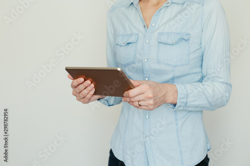 Image of a young woman working on a tablet computer at home on a background of light wall